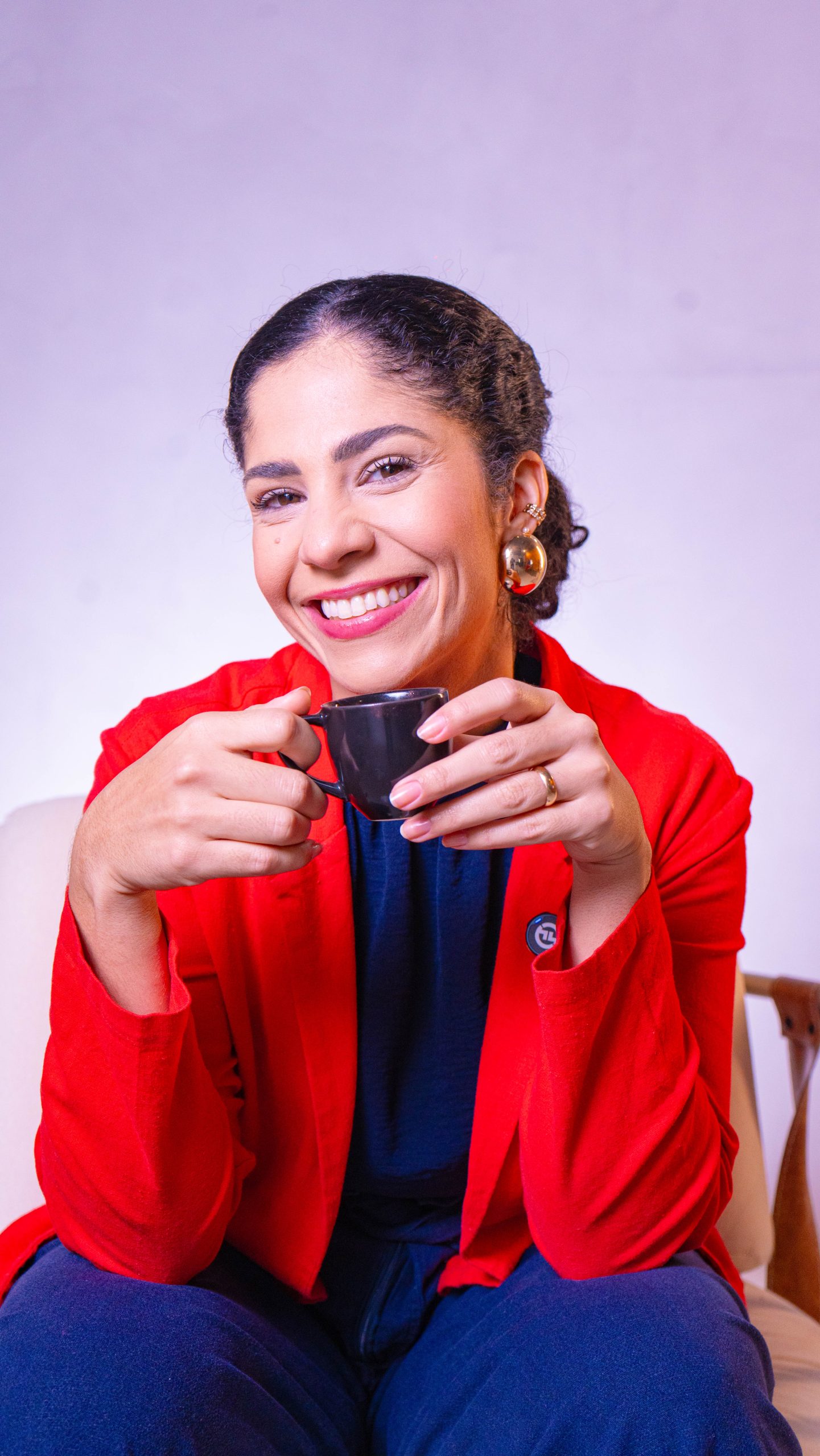 Dra. Sara Dutra segurando uma xícara de café, com blazer vermelho