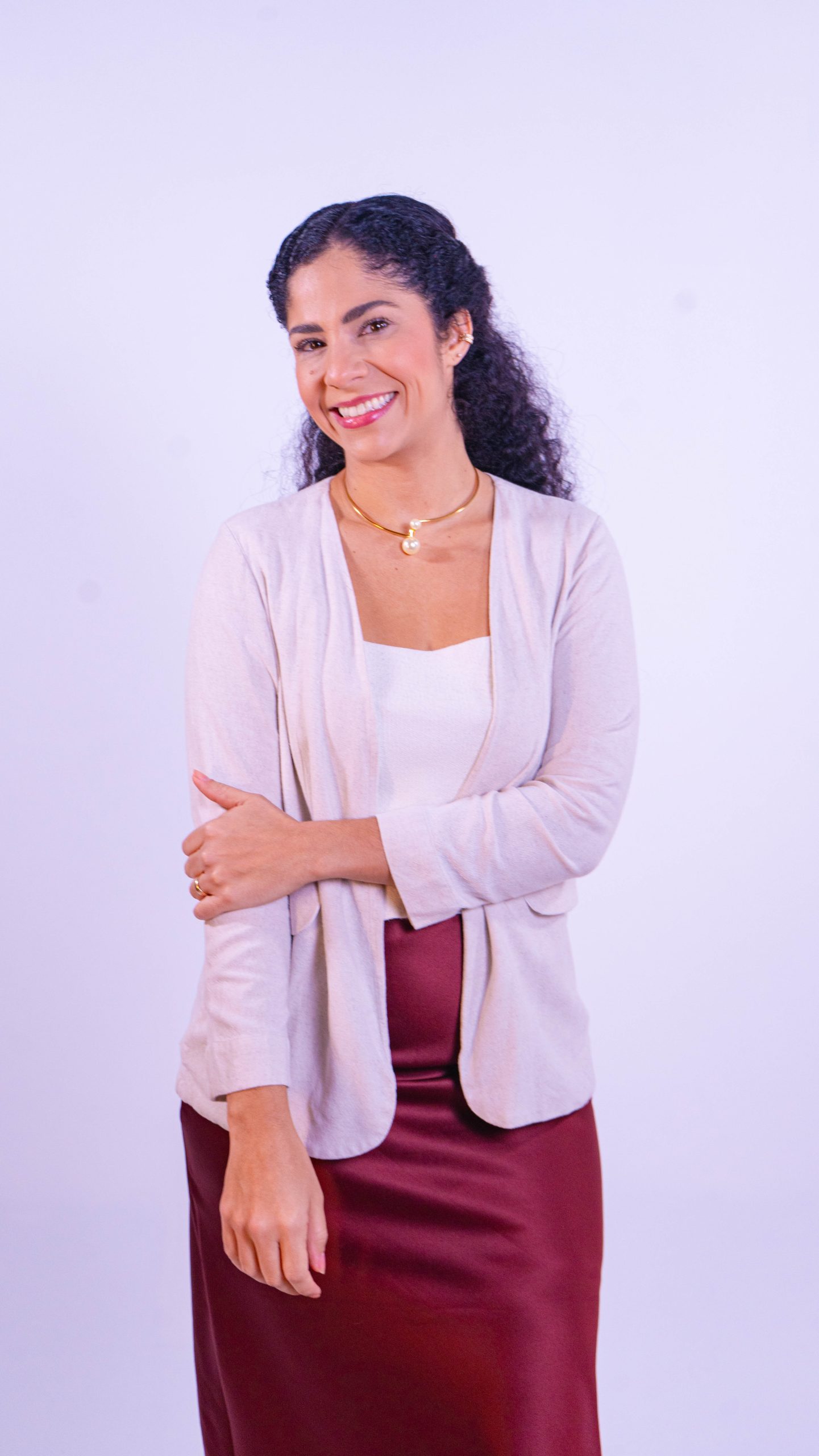 Dra. Sara Dutra de blazer creme e saia vinho, sorrindo em estúdio