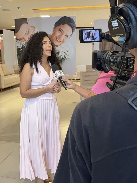 Dra. Sara Dutra dando entrevista à imprensa em frente aos painéis da exposição de retratos